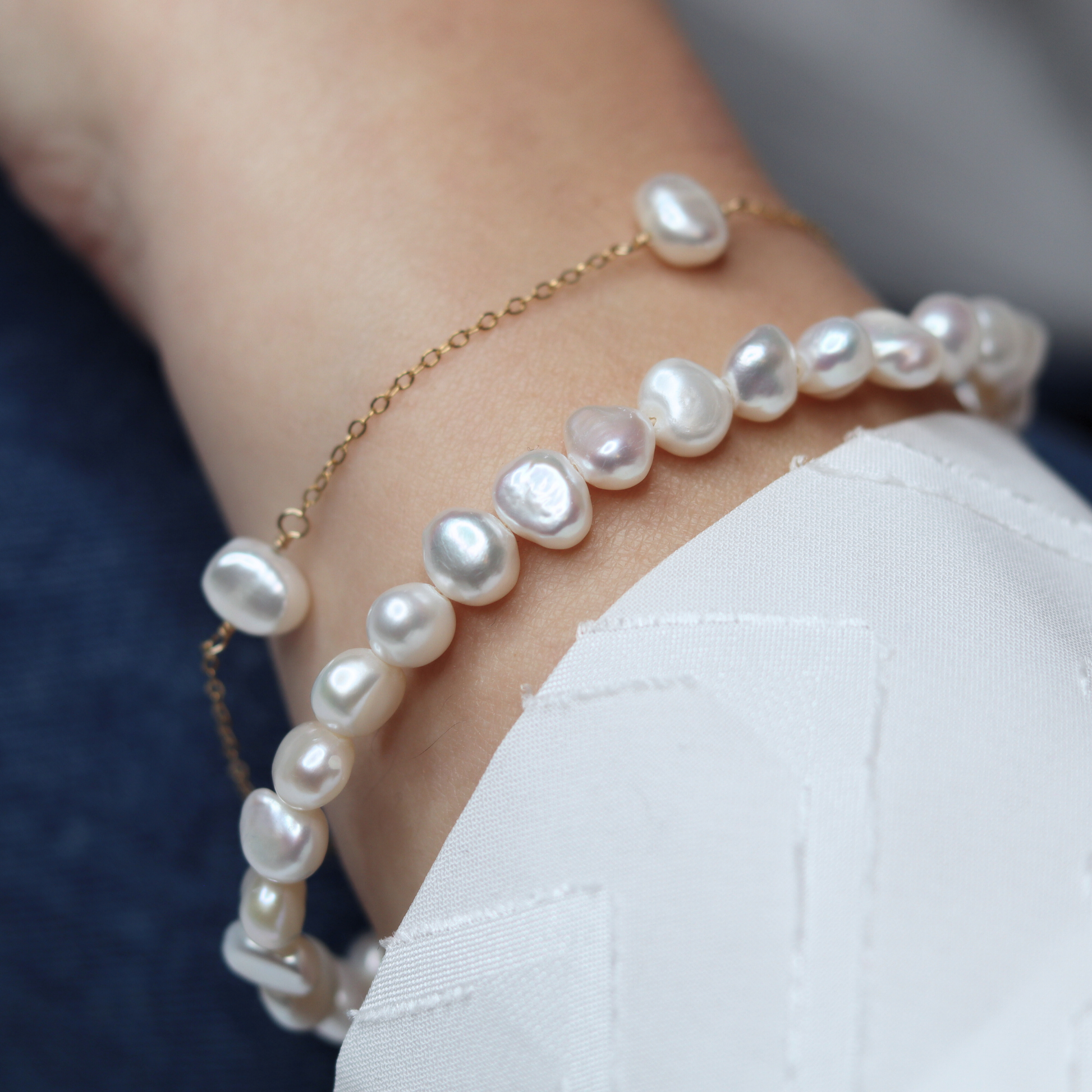 A stylish white baroque pearl bracelet adorned with a gold extension chain, highlighting a refined and contemporary aesthetic.