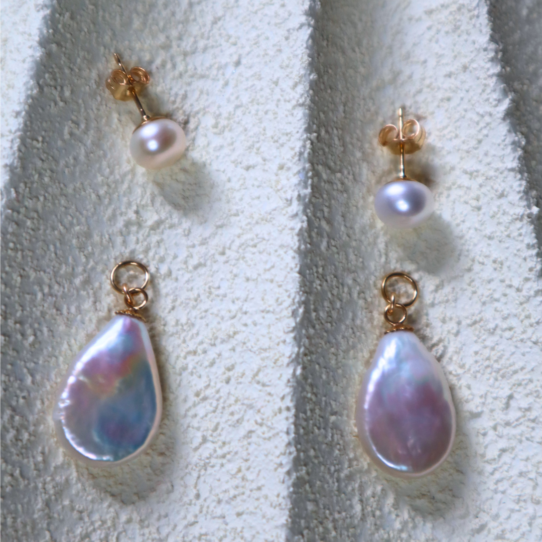 Pair of pearl drop earrings that can be worn as simple studs or with the flat teardrop charms on a textured white surface