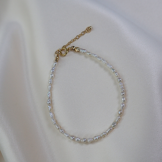 Delicate seed pearl beaded bracelet on a white fabric background