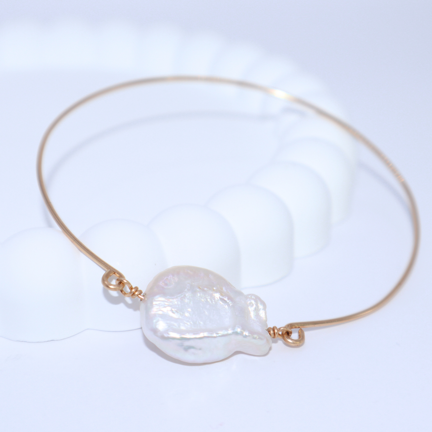 A golden bangle bracelet featuring a single large, baroque pearl, showcasing a blend of luxury and simplicity.