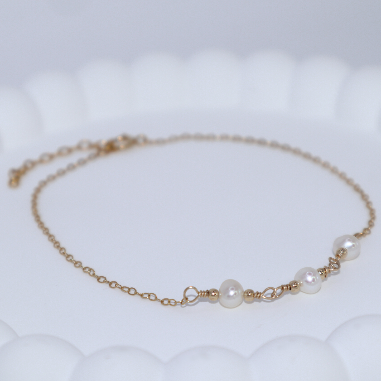 A gold chain bracelet adorned with three elegant pearls surrounded by gold beads, showcasing a blend of luxury and sophistication.