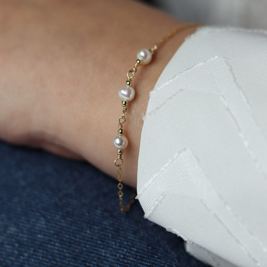 A gold chain bracelet adorned with three elegant pearls surrounded by gold beads, showcasing a blend of luxury and sophistication.