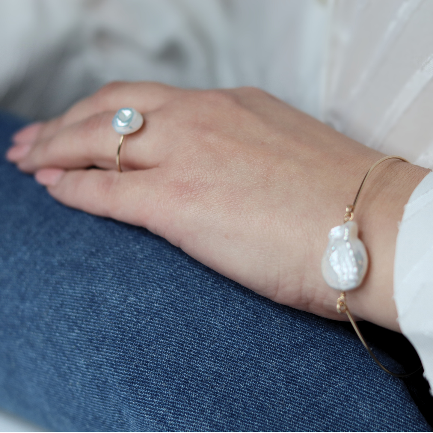 A golden bangle bracelet featuring a single large, baroque pearl, showcasing a blend of luxury and simplicity.