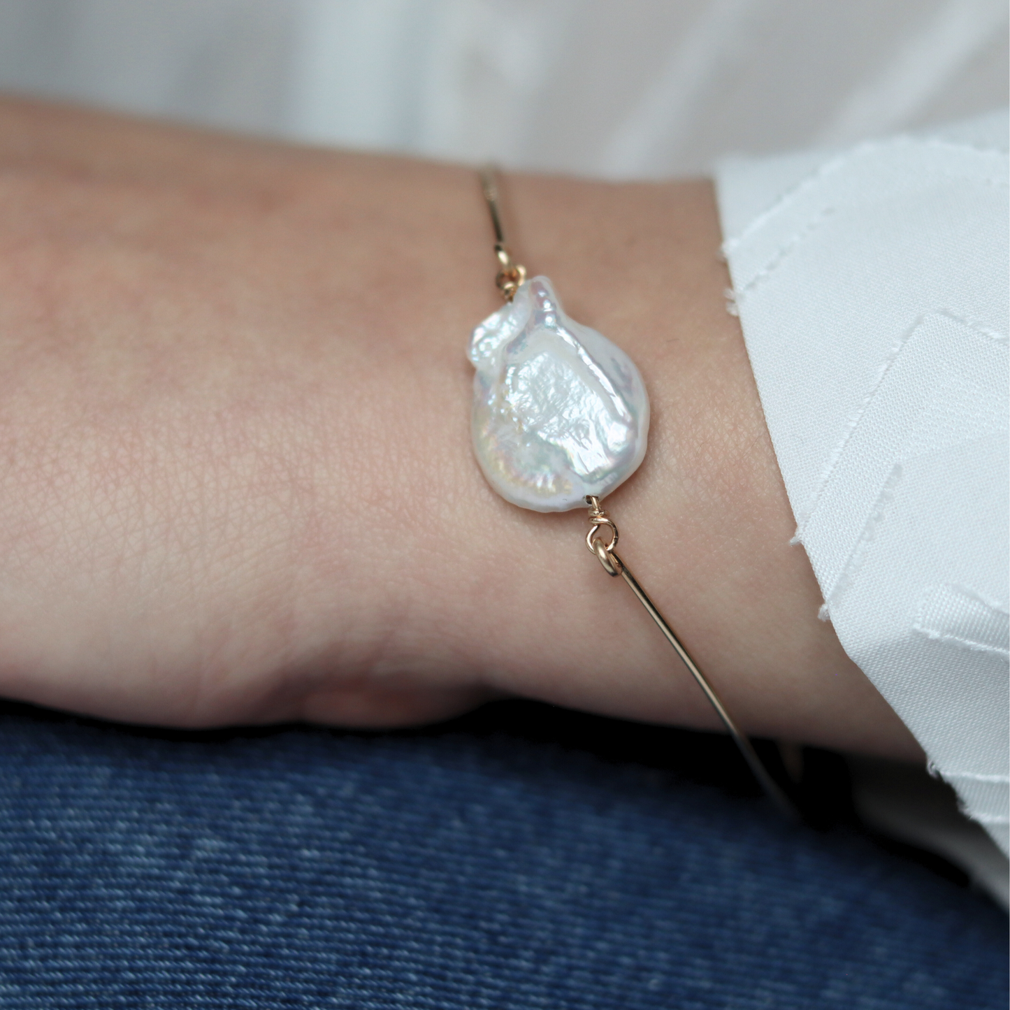 A golden bangle bracelet featuring a single large, baroque pearl, showcasing a blend of luxury and simplicity.