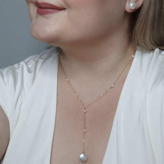 An elegant long necklace adorned with tiny pearls and a large coin pearl pendant, showcasing timeless beauty and luxury, perfect for a deeper cleavage.