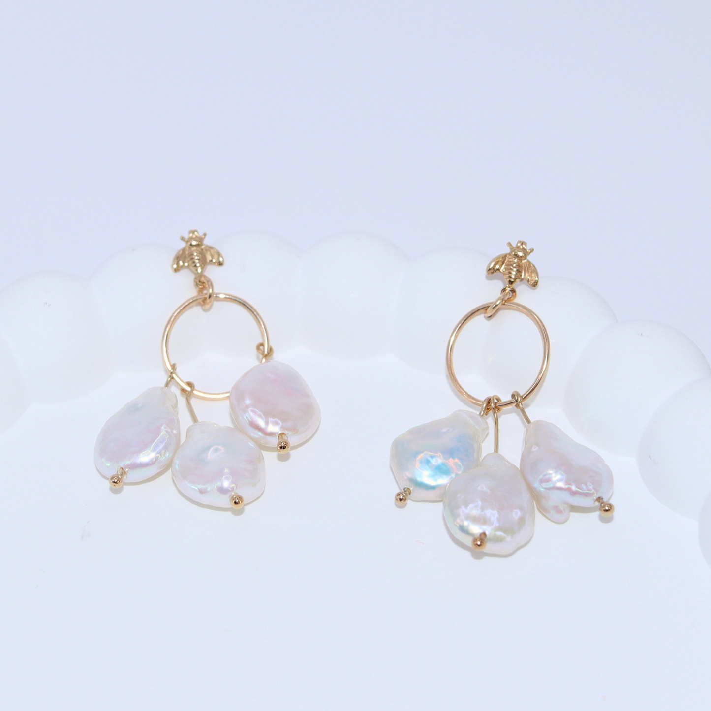 These stunning drop earrings feature a delicate dreamcatcher design, adorned with a bee stud and three luxurious baroque pearls.