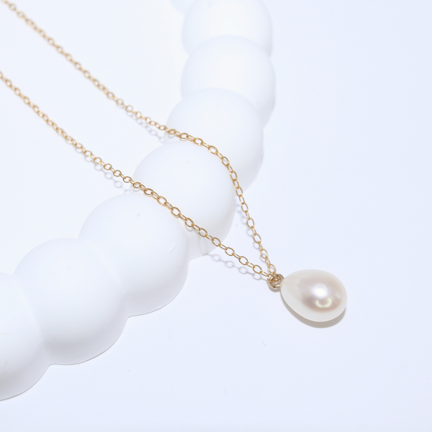 A stunning white teardrop pearl necklace complemented by a gleaming gold chain, embodying elegance and classic style.