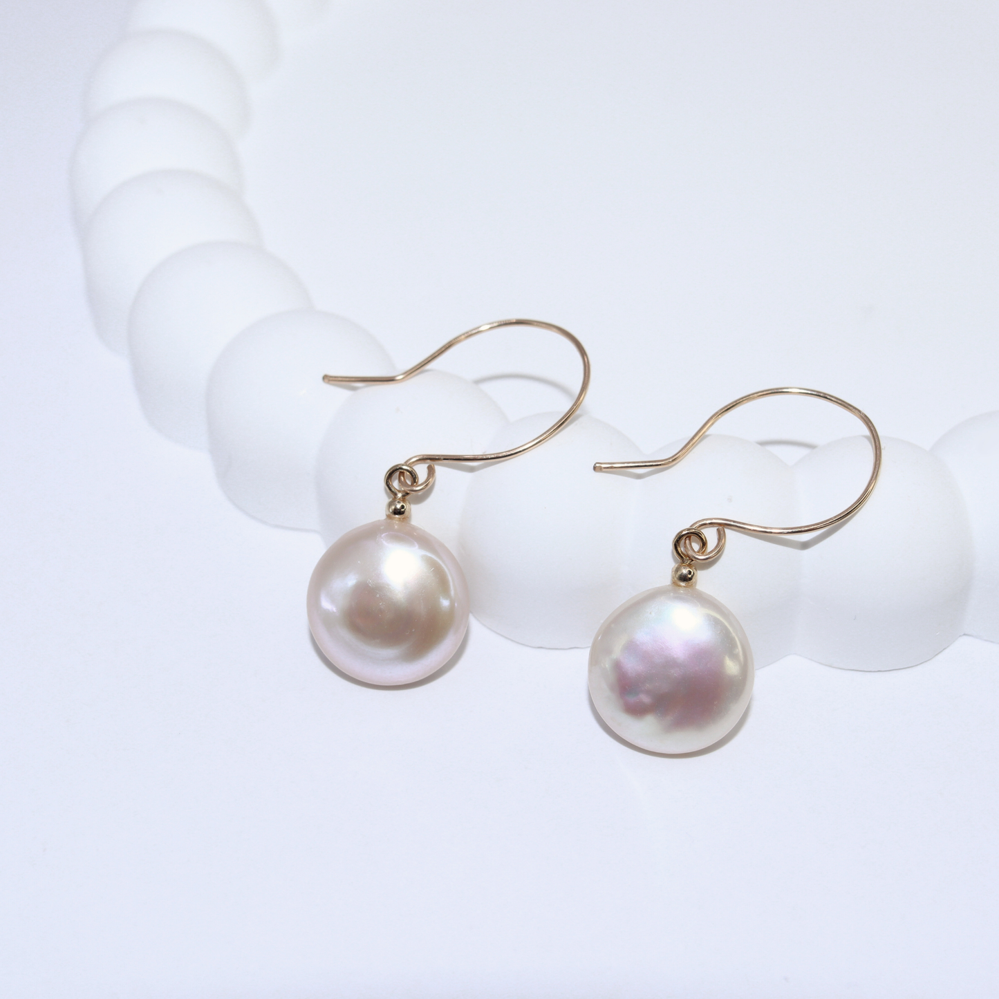 These exquisite earrings feature lustrous coin pearls delicately suspended from round hook earrings.