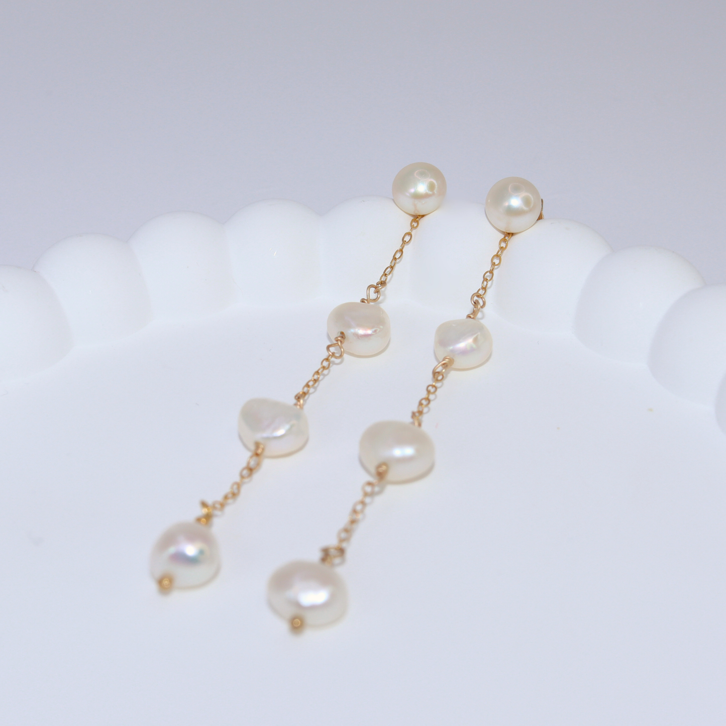 These elegant earrings feature a stud pearl and a delicate chain adorned with three lustrous baroque pearls.
