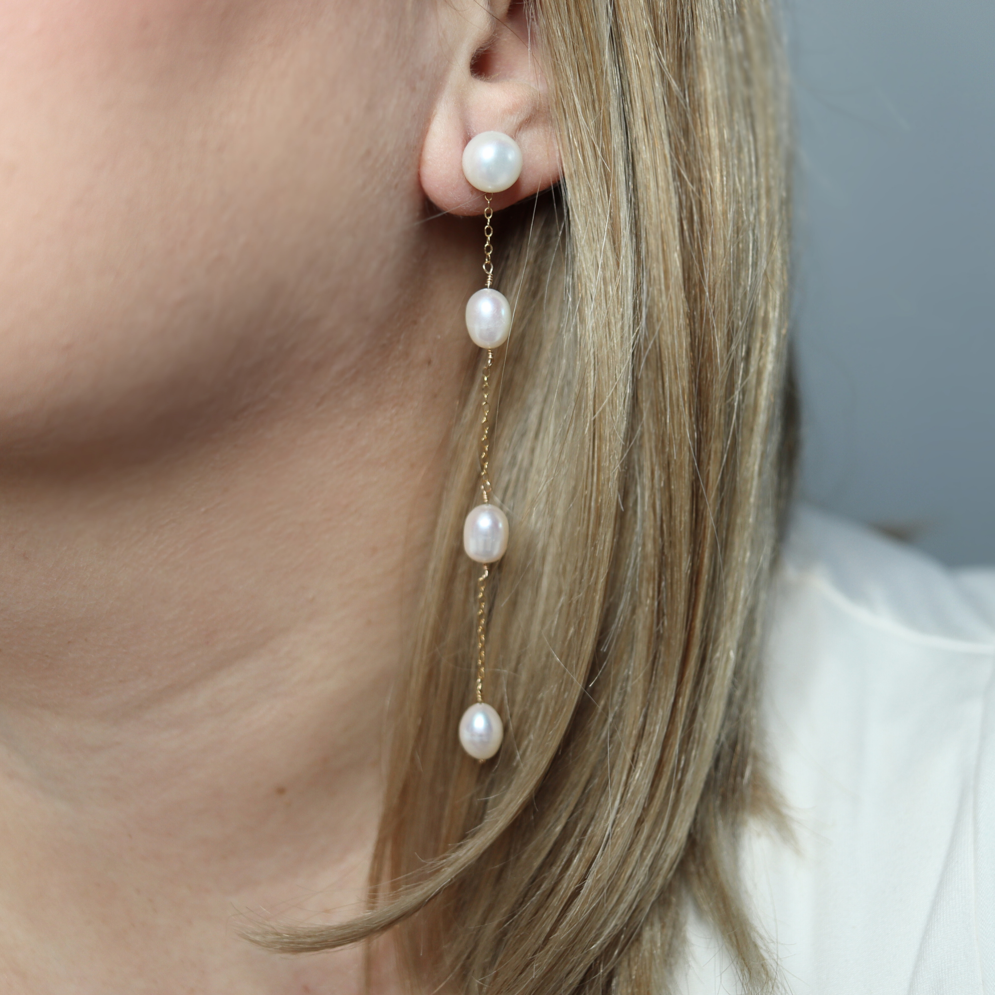 These elegant earrings feature a stud pearl connected to a delicate chain adorned with three rice pearls, creating a beautiful and unique look.