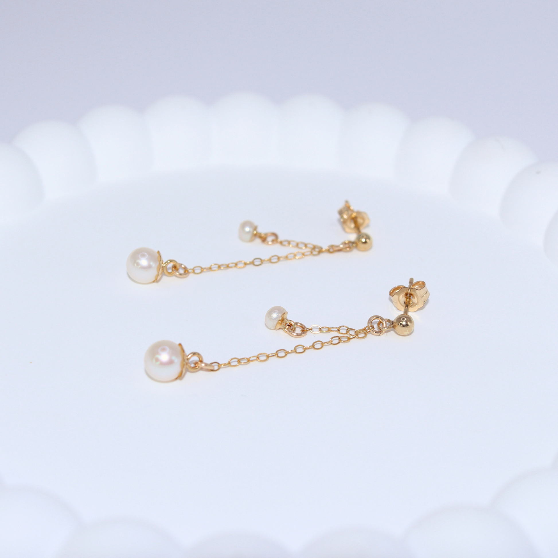 Made with two small pearls delicately dangling on dainty chains, these ball stud earrings add a touch of sophistication to any outfit.