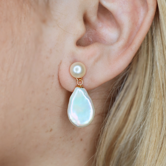 Pearl and teardrop-shaped earring worn by a person with blonde hair.