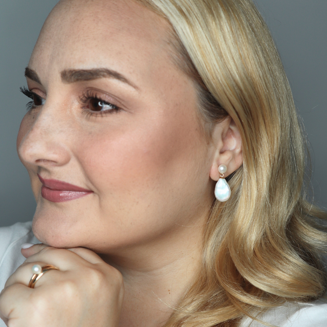 Woman wearing pearl earrings and a ring with a neutral background