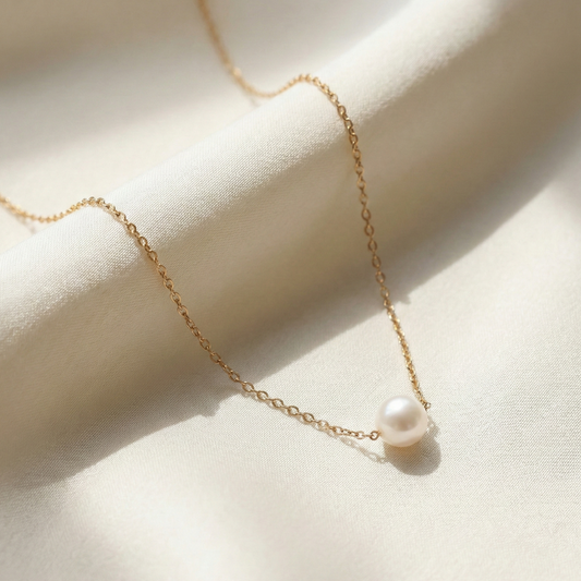 Gold necklace with a single pearl pendant on a light fabric background