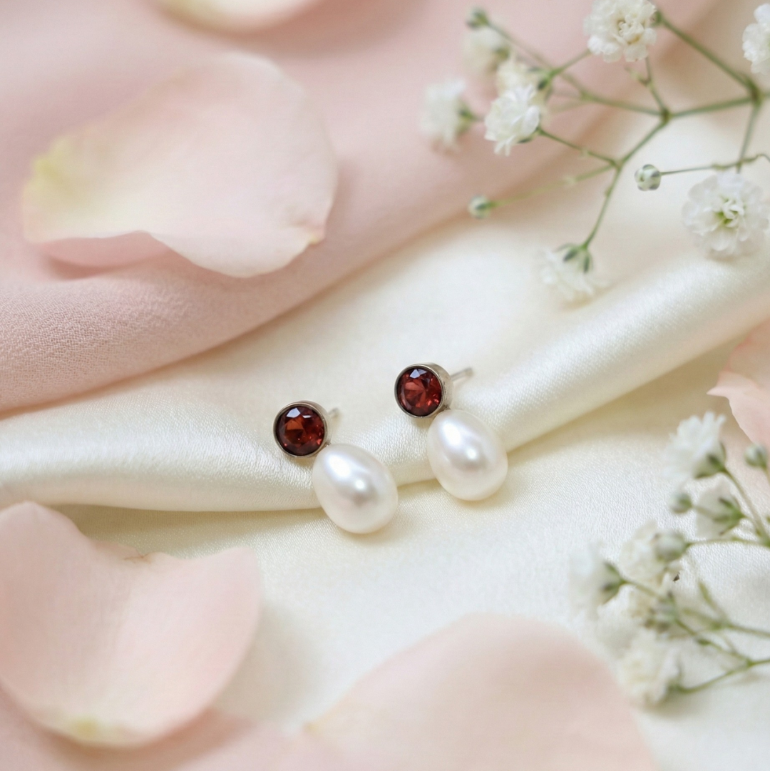 Pearl earrings with red gemstones on a pink fabric background with flowers