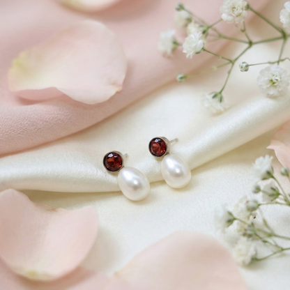 Pearl earrings with red gemstones on a pink fabric background with flowers
