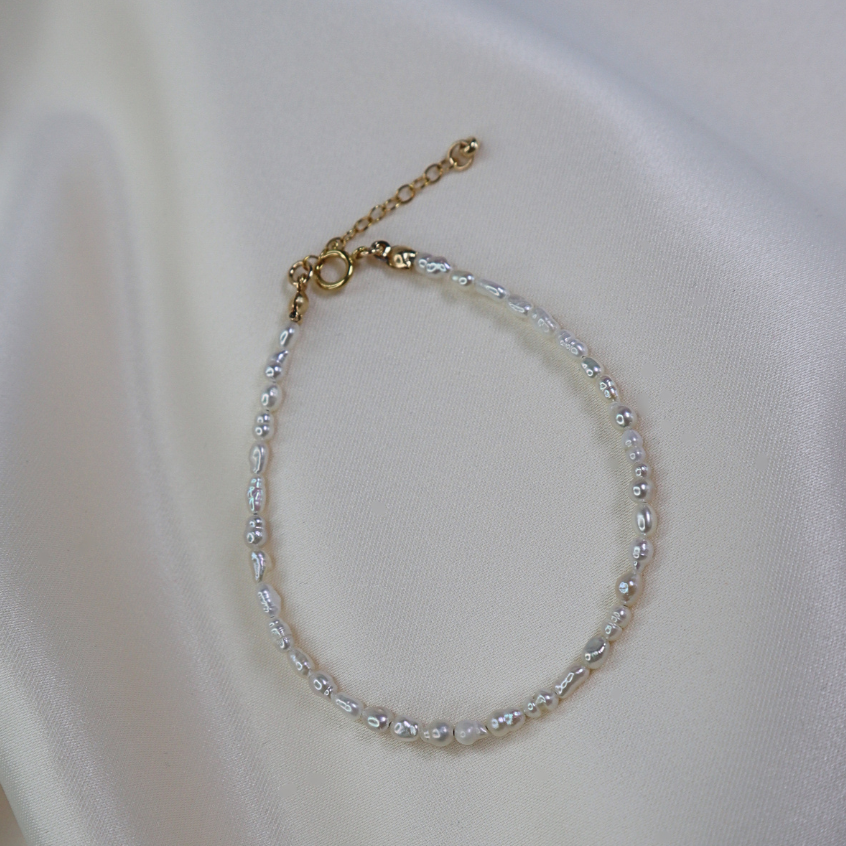 Delicate seed pearl beaded bracelet on a white fabric background