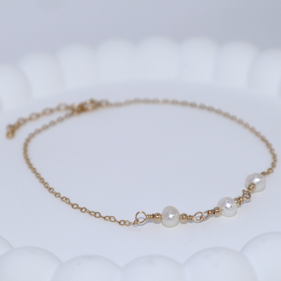 A gold chain bracelet adorned with three elegant pearls surrounded by gold beads, showcasing a blend of luxury and sophistication.