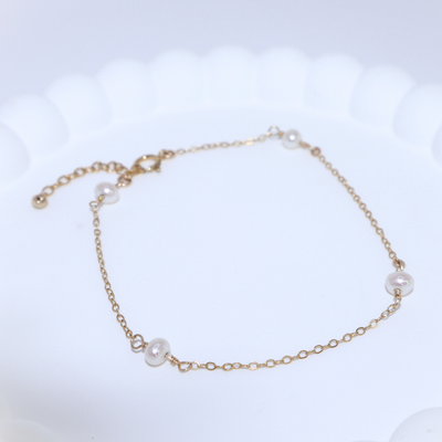 A gold chain bracelet adorned with four elegant pearls, showcasing a blend of luxury and sophistication.