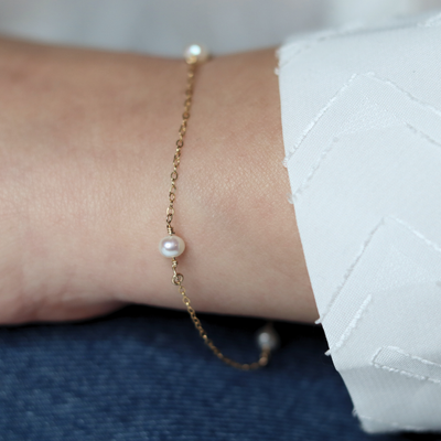 A gold chain bracelet adorned with four elegant pearls, showcasing a blend of luxury and sophistication.
