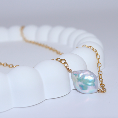 A delicate pearl necklace featuring a baroque pearl elegantly suspended on a gold chain, showcasing timeless beauty.
