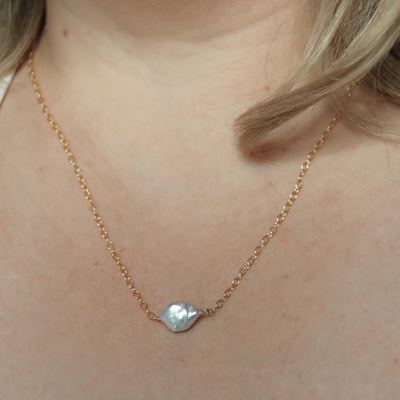 A delicate necklace featuring a baroque pearl elegantly suspended on a gold chain, showcasing timeless beauty.