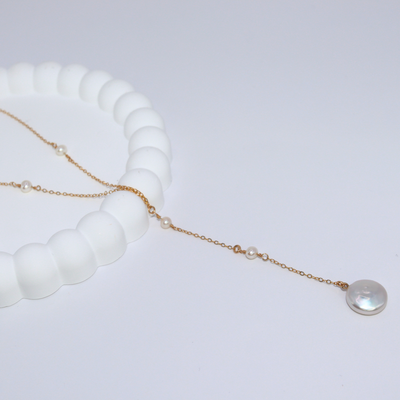 An elegant long necklace adorned with a tiny pearls and a large coin pearl pendant, showcasing timeless beauty and luxury, perfect for a deeper cleavage. 