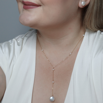An elegant long necklace adorned with tiny pearls and a large coin pearl pendant, showcasing timeless beauty and luxury, perfect for a deeper cleavage. 