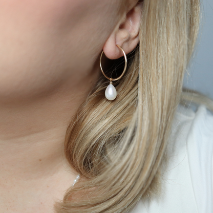  These sophisticated hoop earrings feature a single teardrop pearl, adding a touch of elegance to any outfit. 