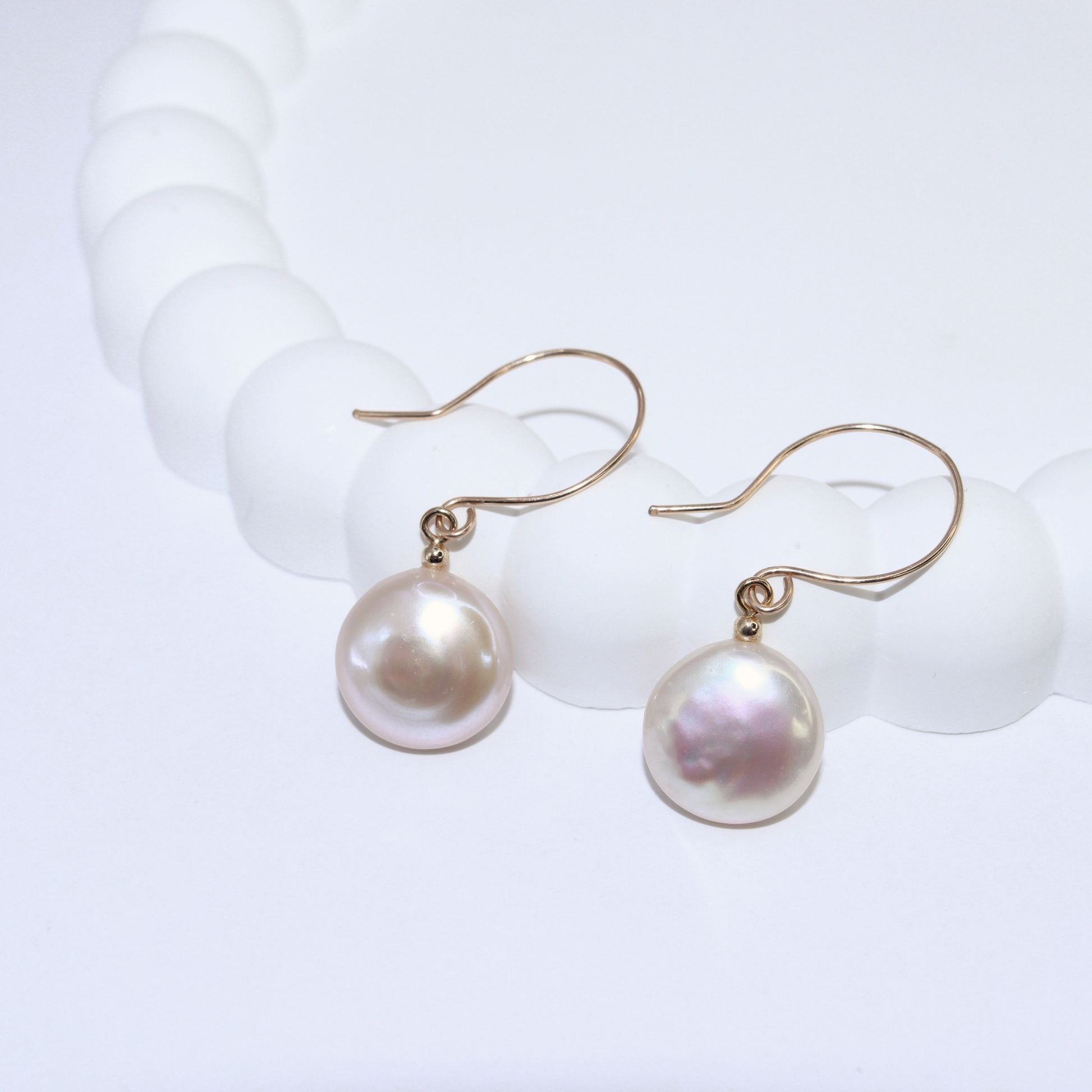 These exquisite earrings feature lustrous coin pearls delicately suspended from round hook earrings.
