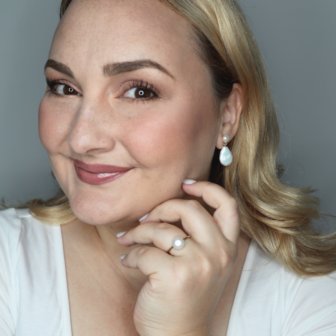 Woman wearing pearl drop earrings and a pearl ring, with a neutral background