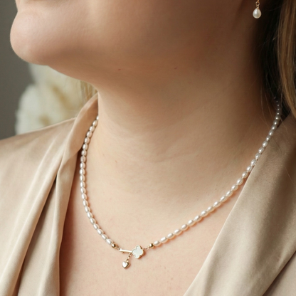 Close-up of a woman wearing a pearl necklace with a key and heart locket charm and pearl earrings with a neutral background