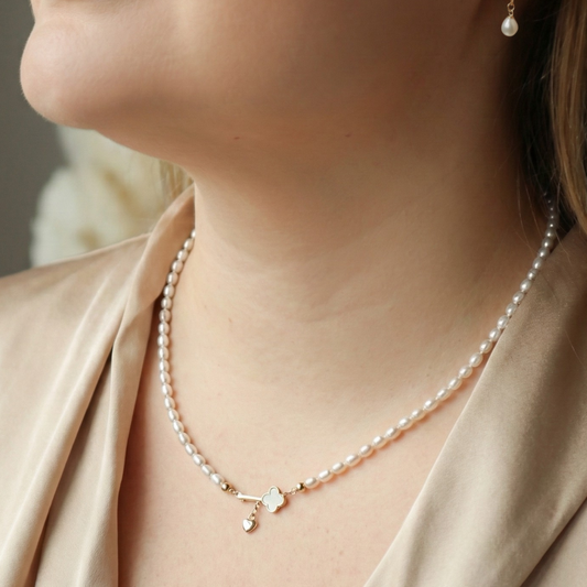 Close-up of a woman wearing a pearl necklace with a key and heart locket charm and pearl earrings with a neutral background